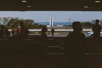Silhuetas de pessoas em uma passagem subterrânea, com o Congresso Nacional ao fundo, em Brasília.