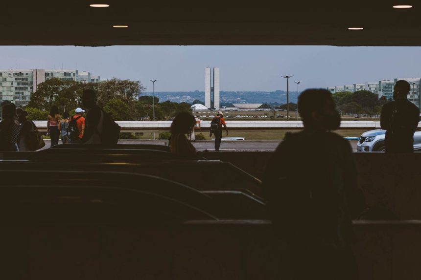 Silhuetas de pessoas em uma passagem subterrânea, com o Congresso Nacional ao fundo, em Brasília.