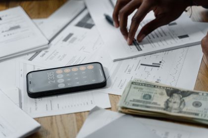Mãos sobre uma mesa com smartphone, dinheiro, relatórios financeiros e calculadora