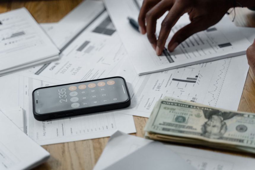 Mãos sobre uma mesa com smartphone, dinheiro, relatórios financeiros e calculadora