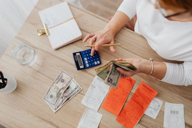 Pessoa usando uma calculadora para organizar dinheiro e recibos sobre uma mesa.